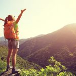 cheering woman hiker open arms at mountain peak cliff